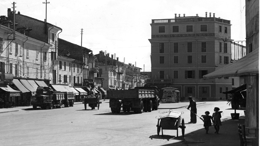 Pavia, Borgo Ticino, piazzale Ghinaglia veduta d'assieme, a sinistra la drogheria Albani e la trattoria Ferrari, sullo sfondo il palazzo sede del pastificio Marozzi, 1934  (CHL MC_19394)